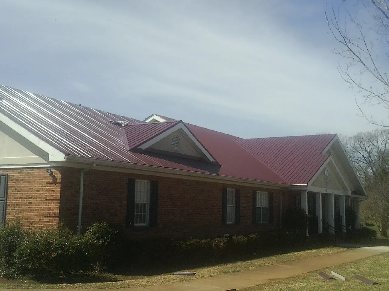 Red metal roof with gabled entries on a long brick building, from a Hail Damage Roof Repair job in Galveston