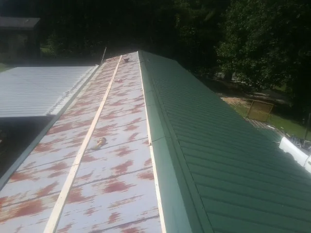 Old rusted panels beside newly installed green metal roofing — Wind Damage Roof Repair by Roofing Brothers in Galveston
