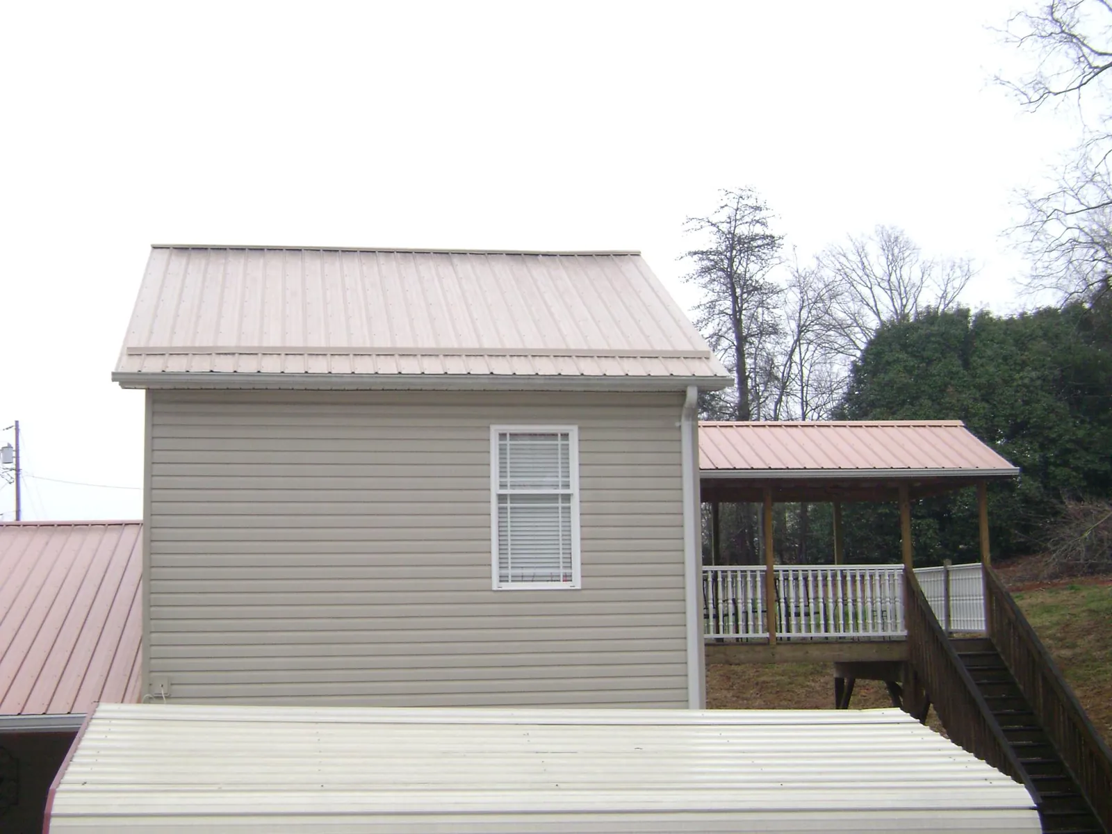 Tan metal roofs on a two story addition and attached porch, from a Roof Replacement job in Galveston